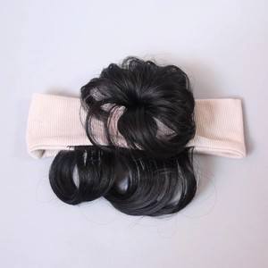 Detailed macro view of curly synthetic hair bun attached to a soft knitted baby headband