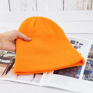 Detailansicht der dicken orangefarbenen Strickmütze auf weißem Holzuntergrund