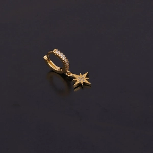 Boucle d'oreille dorée avec pendentif étoile en zircon sur une surface réfléchissante