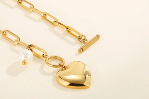 Détail du pendentif cœur doré avec perle et fermoir OT sur une chaîne en acier