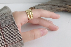 Close-up of gold irregular hammered texture ring on model finger with minimalist wood accent