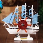 Détail d'un voilier miniature en bois avec voiles bleues, gouvernail rouge et ancre