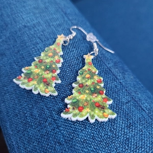 Macro shot of festive Christmas tree earrings made of acrylic on a blue fabric surface