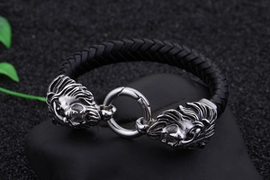 Nahaufnahme des geflochtenen Lederarmbandes mit zwei Löwenköpfen auf dunklem Stein