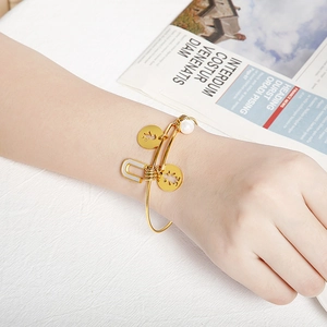 Golden stainless steel bangle with shell charms featuring letter U and figure silhouettes