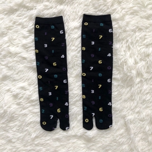Detail view of black tabi socks with colorful digital patterns on white plush background