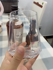 Detailed close-up of a hand holding a geometric faceted clear glass cup for cold drinks