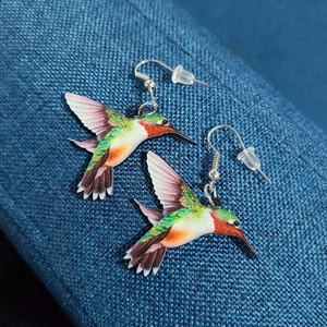 Colorful hummingbird acrylic drop earrings with silver hooks on dark fabric background