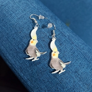 Close-up of acrylic cockatiel bird earrings with silver hooks on blue textured fabric
