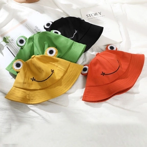Flat lay of colorful frog bucket hats in green, yellow, red, and black on white fabric