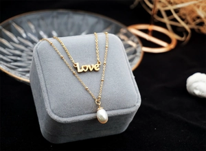 Detail of layered gold titanium necklace with Love pendant and teardrop pearl on velvet box