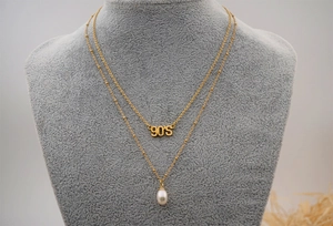 Detail of layered gold necklace featuring 90'S letter pendant and oval white pearl
