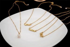 Detail of four golden layered necklaces featuring Love, Happy, and 90s letter pendants