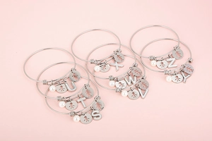 Detailed macro view of silver steel bangles with alphabet charms and shell accents