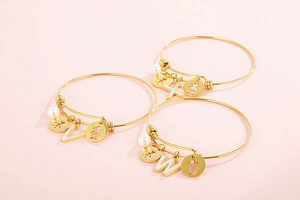 Detailed shot of golden alphabet bracelets with white pearl and child silhouettes charms