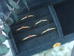 Close-up of five minimalist gold rings with colorful gemstones in a blue velvet box