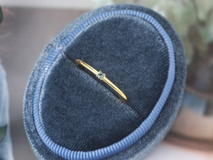 Close-up of minimalist gold ring with small light blue zircon set in navy velvet box