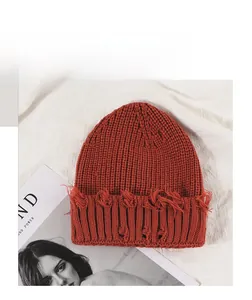 Détail du bonnet en maille rouille avec bords effilochés et texture chaude et douce