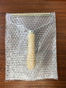 Manual lint remover with wooden handle shown in protective bubble wrap packaging