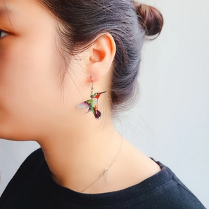 Colorful laser-cut acrylic hummingbird earrings worn by a model in a close-up profile view