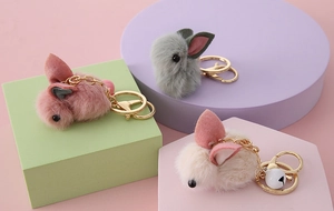 Detailed view of plush bunny keychains in pink, grey, and beige with golden metal rings