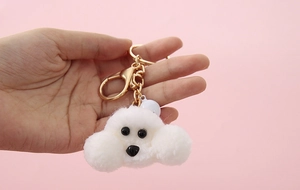 Close-up of white plush puppy keychain with golden ring and small bell detail