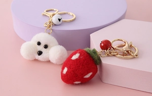 Detail of wool felt keychains featuring a white puppy and red strawberry with golden bells