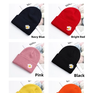 Detail view of colorful knitted beanies with white daisy embroidery and ribbed cuffs