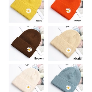 Detail of colorful knit beanies featuring white daisy embroidery in a grid layout
