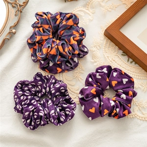 Close-up of three purple velvet Halloween scrunchies with orange and white patterns