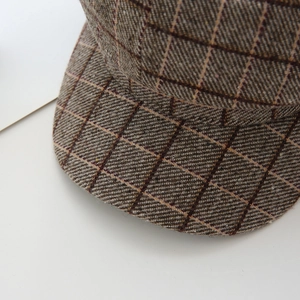 Close-up of brown plaid wool texture and stitching on the brim of an octagonal cap