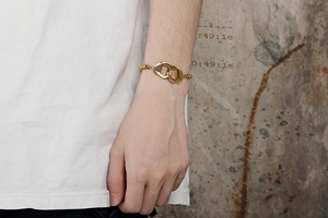 Detail of a gold bead bracelet featuring unique interlocking handcuffs on a wrist