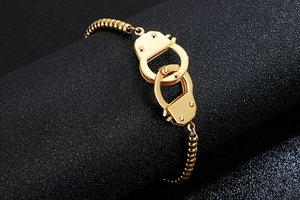 Macro detail of golden handcuff pendant and bead chain on a textured black display