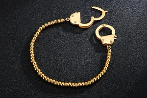 Detail of golden beaded bracelet with unique handcuff clasp on black background