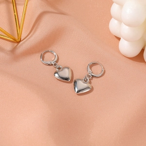 Détail de boucles d'oreilles cœur argentées sur soie rose avec finition métallique