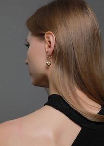 Vue macro des boucles d'oreilles cœur dorées montrant la tenue réelle et l'éclat métal