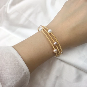 Three-layer gold spiral wire wrap bracelet with white and pink pearls on silk background