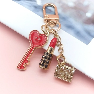 Detail of creative keychain with red heart, mini lipstick and golden handbag charms