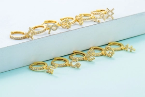 Detailed view of gold hoop earrings with white zircon pavé and zodiac symbol pendants