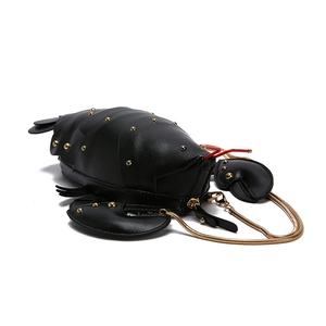 Detail of beetle shaped crossbody bag featuring gold rivets and red antennae accents