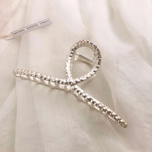 Close-up of a silver metal claw clip with a hammered texture on white fabric