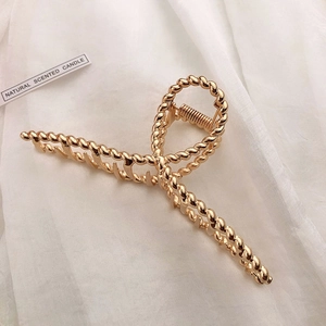 Detailed close-up of large golden metal claw clip with elegant twisted texture design