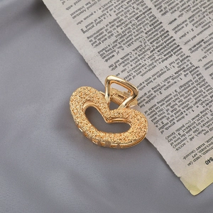 Macro detail of gold heart-shaped metal hair claw with embossed floral patterns