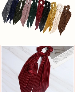 Macro detail of wine red corduroy bow scrunchie with long ribbons on marble background