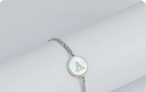 Détail macro du bracelet en acier argenté avec pendentif en nacre et lettre A ajourée