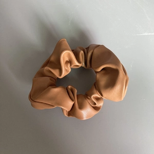 Detailed texture of a camel brown faux leather scrunchie with soft aesthetic pleats