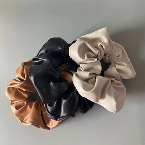 Close-up of three faux leather scrunchies in brown, black, and beige with smooth texture