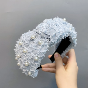 Detail of light blue feather yarn headband with embedded pearls held against a grey wall