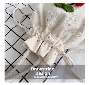 Detailed close-up of cherry and daisy embroidery on a cream canvas drawstring bucket bag