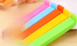 Five colorful 11cm plastic sealing clips in pink, blue, orange, yellow, and green on wood